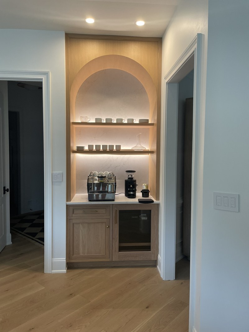 Arched beverage nook with illuminated shelves, a wood lower cabinet and an under-counter beverage refrigerator.