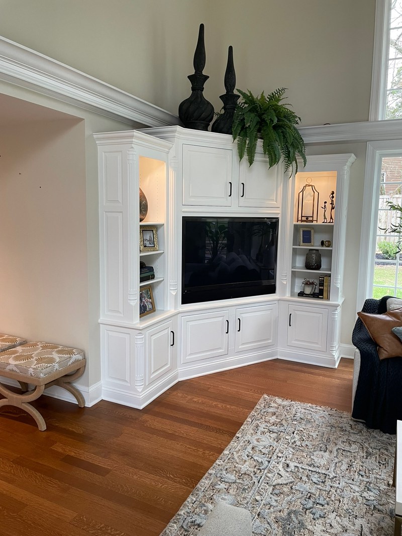 White corner media cabinetry with a television, lower cupboards and lit glass-front display shelves.
