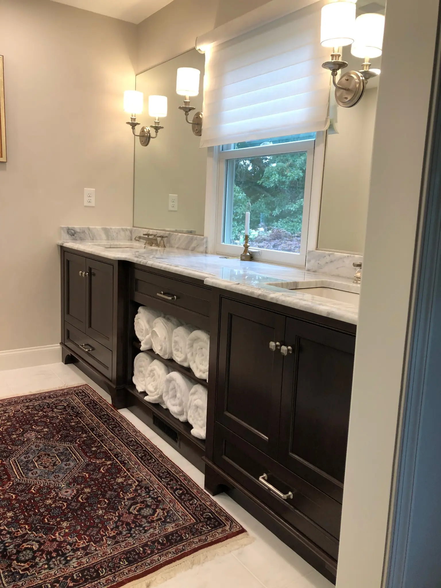 Dark double bathroom vanity with paneled doors, lower drawers and open center shelves filled with rolled towels.