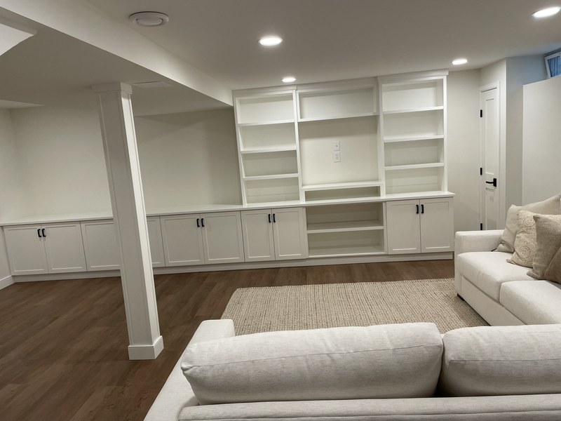 White built-in wall unit with open shelves and lower cabinets behind a light-colored sectional sofa.