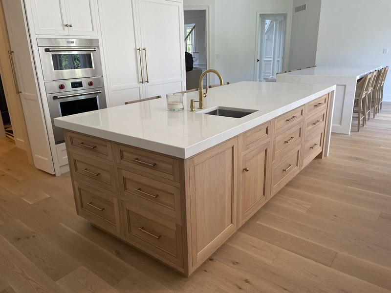 Natural wood kitchen island with paneled doors, drawers, a white countertop and an inset sink.