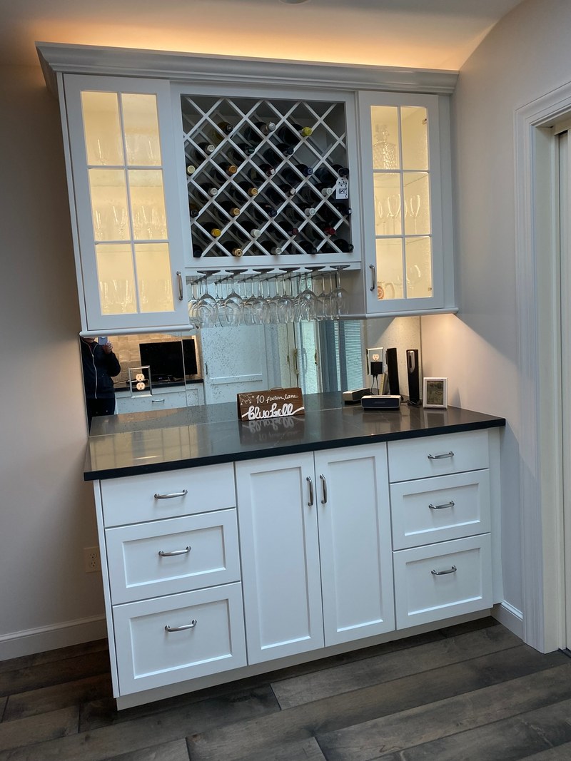 Painted beverage cabinet with an upper wine rack, lit glass-front doors, a dark counter and lower drawers.