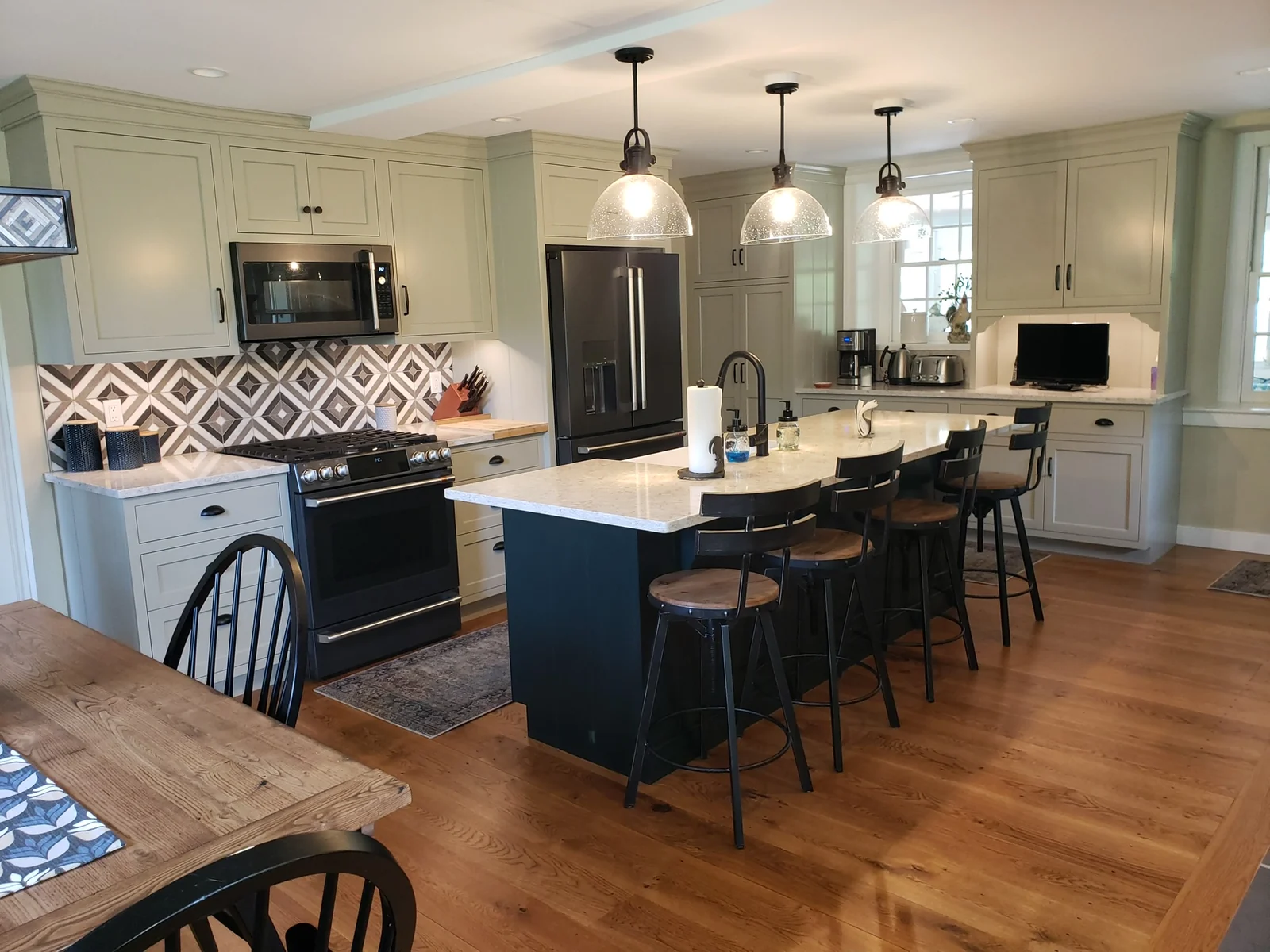 Light painted kitchen cabinets with a dark island, pendant lights and patterned backsplash.