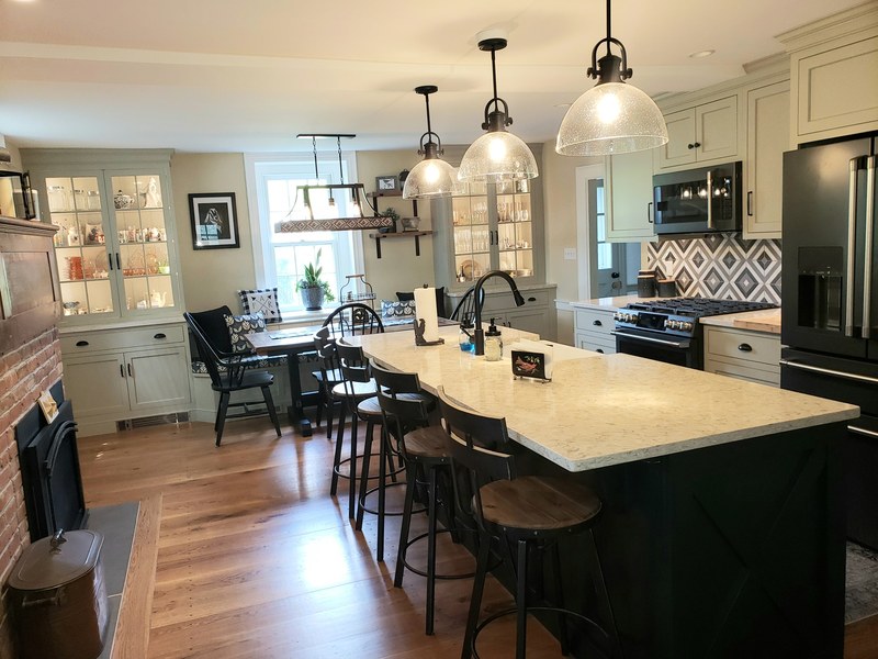 View along a light kitchen island countertop with a sink, dark base cabinets and pendant lighting.