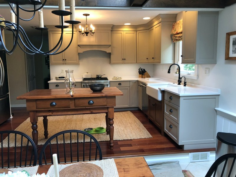 Kitchen with painted upper cabinets, a white farmhouse sink, wood furniture and a dark hanging light fixture.