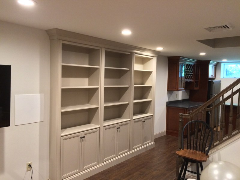 White built-in shelves with lower cabinets and drawers beside a wood stair railing.