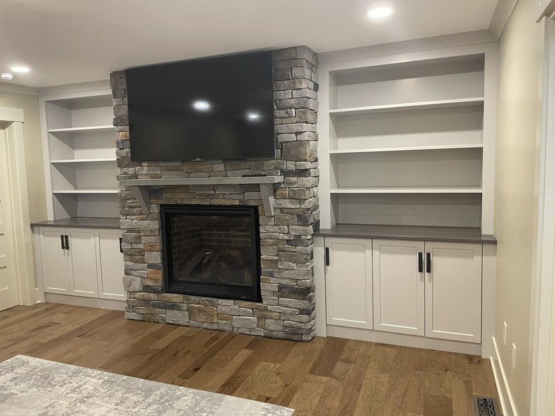 White cabinets and open shelves on both sides of a stone fireplace with a television above.