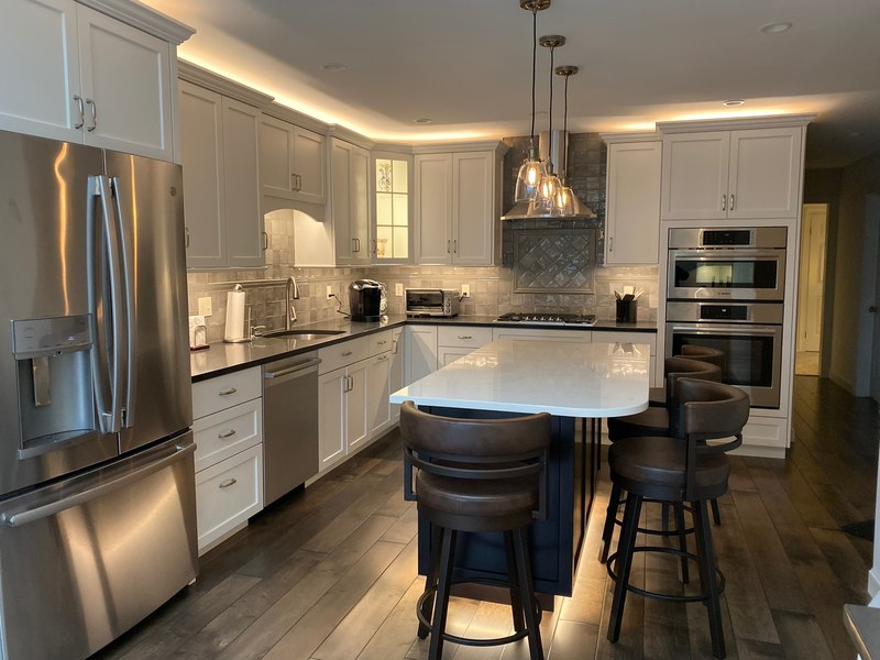 White kitchen cabinets, stainless steel appliances and a light island countertop with two dark stools.