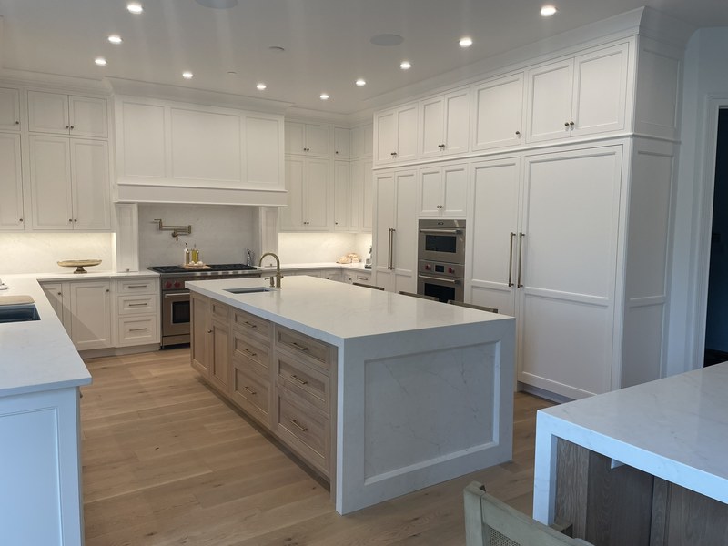 White kitchen cabinets surrounding a natural wood island with a light countertop and sink.