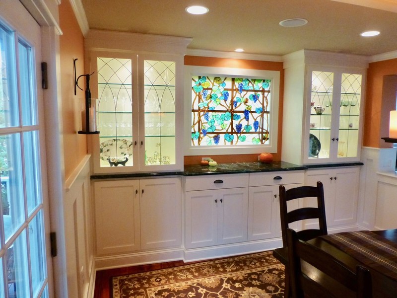 White lower cabinets beneath a stained-glass window, with glass-front upper cabinets on either side.