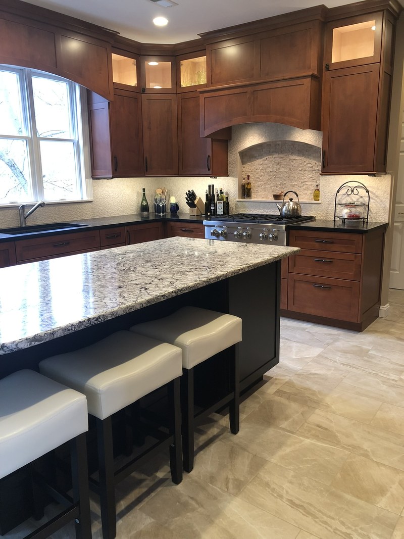 Dark wood kitchen cabinetry with illuminated upper display doors and two stools beneath the island countertop.