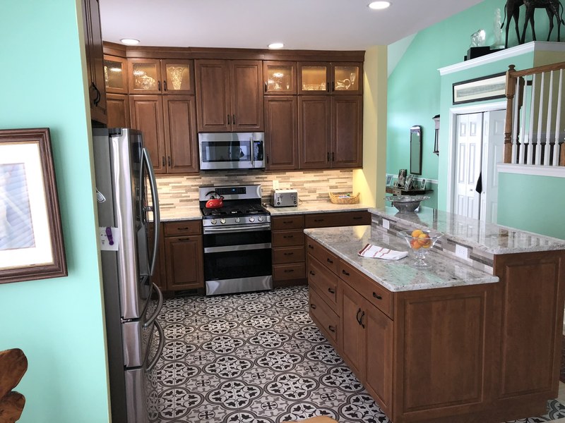 Dark wood kitchen cabinets with a paneled island, window over the sink and patterned floor.