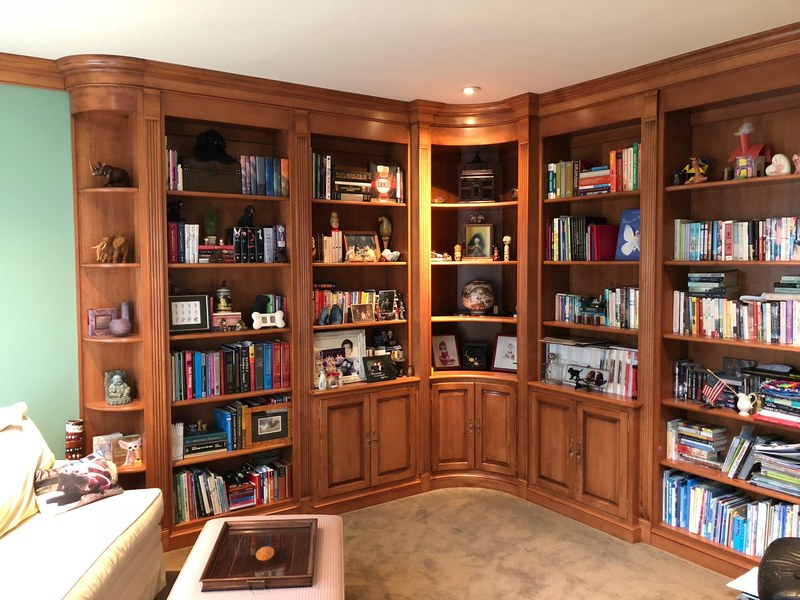 Wood bookcases filled with books, with lower cabinets and illuminated display shelves around a corner.